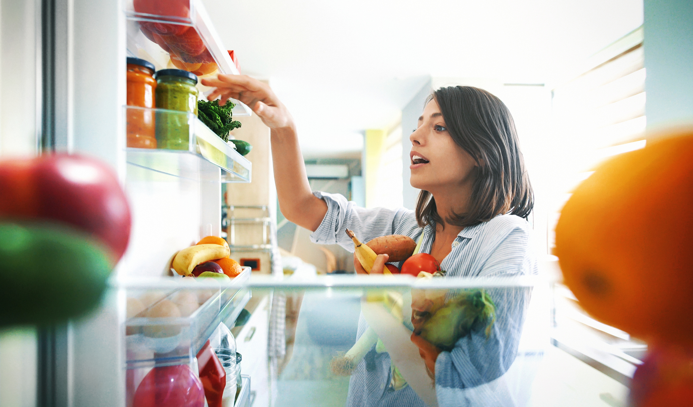 woman putting away produce in fridge